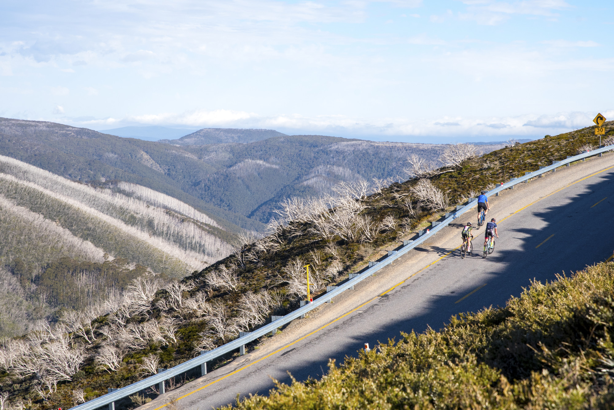 Group of cyclists riding up the Mt Hotham 7 Peaks Challenge road climb with mountain views in the background