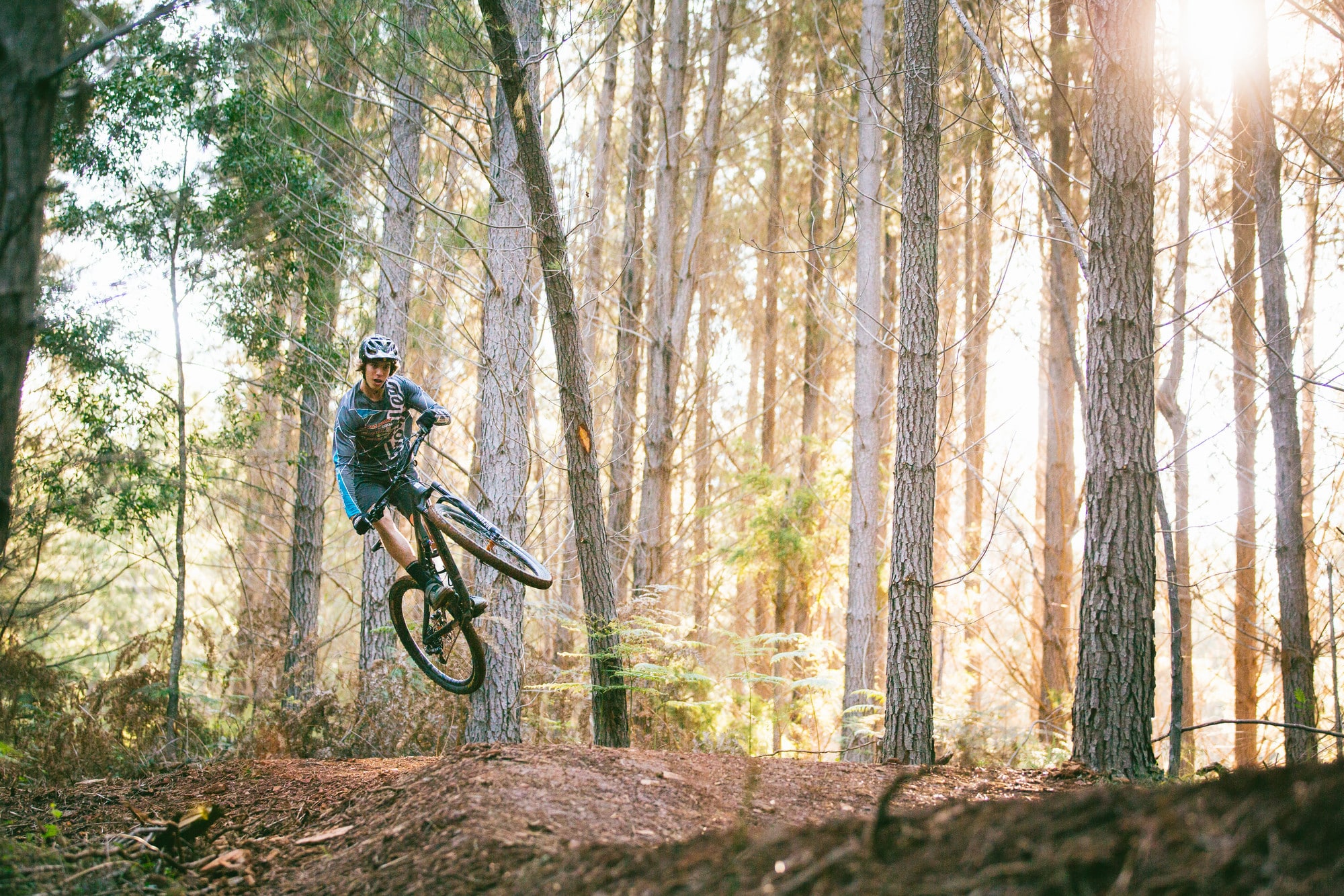 Cyclist riding berms and jumping through the pine trees at Mystic Bike Park