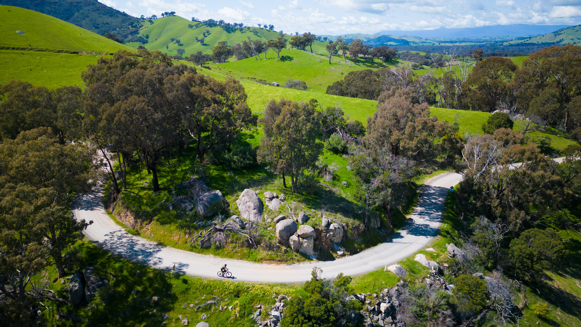 Cyclist rolling past green hills and granite rocks on Yea's gravel roads