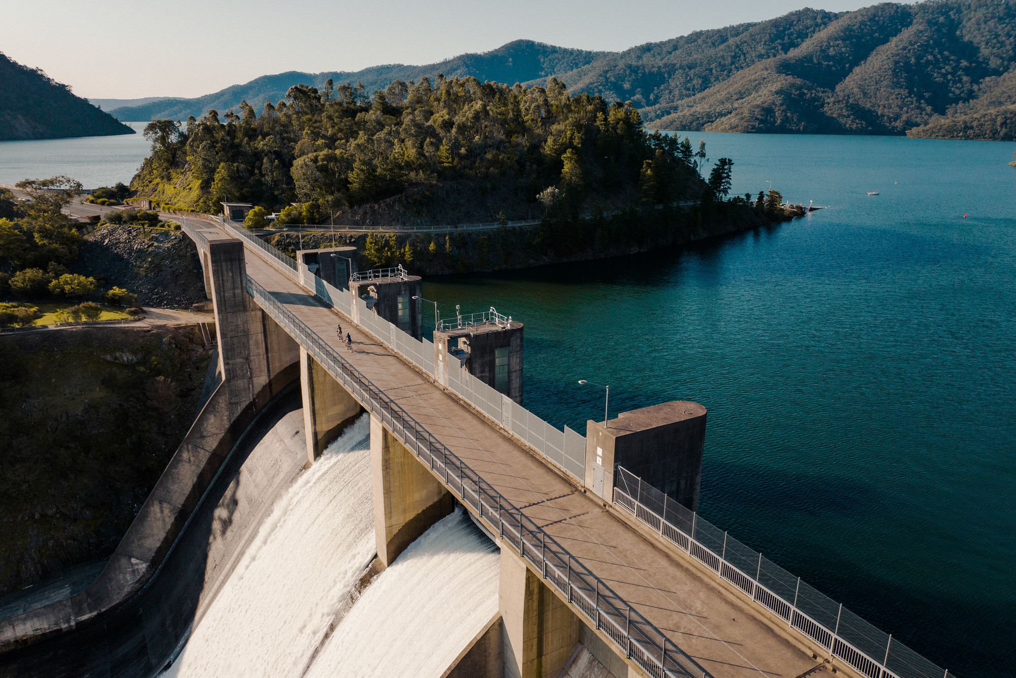 Two cyclists riding over Lake Eildon dam with views of the water and mountains