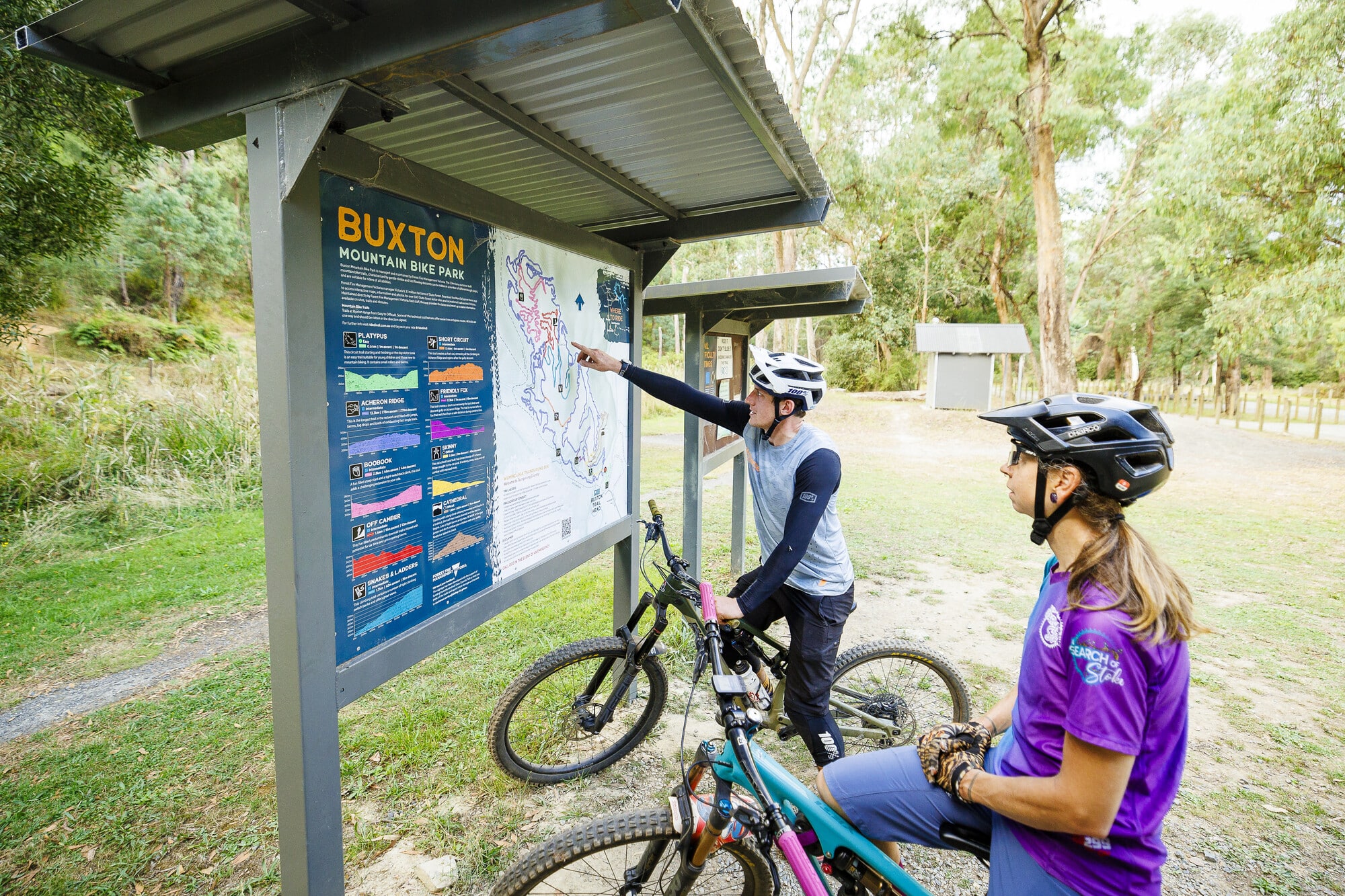 Two cyclists reading the trailhead map at Buxton MTB Park