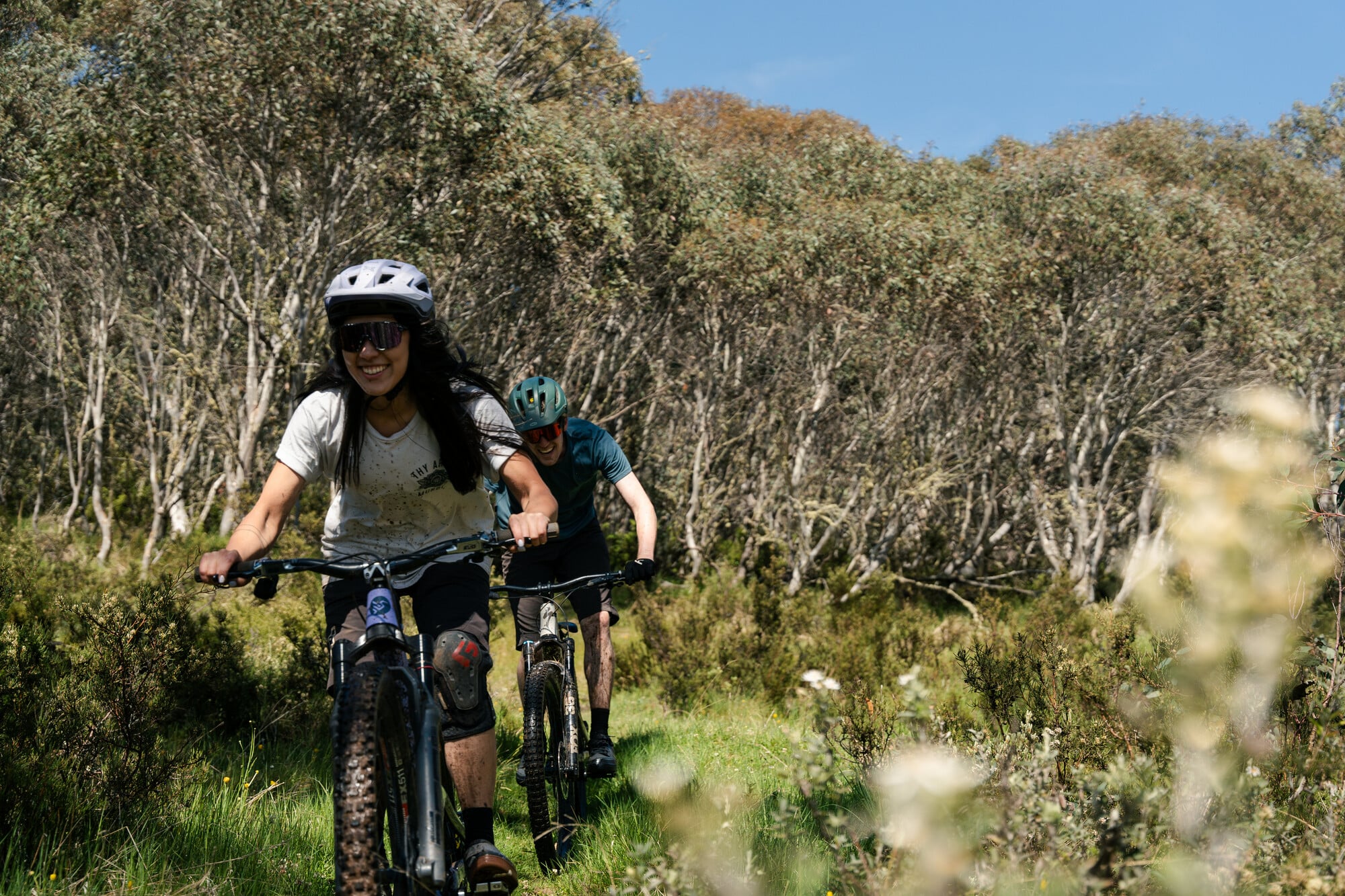 Two cyclists smiling as they ride through the gum trees at Dinner Plain MTB Park