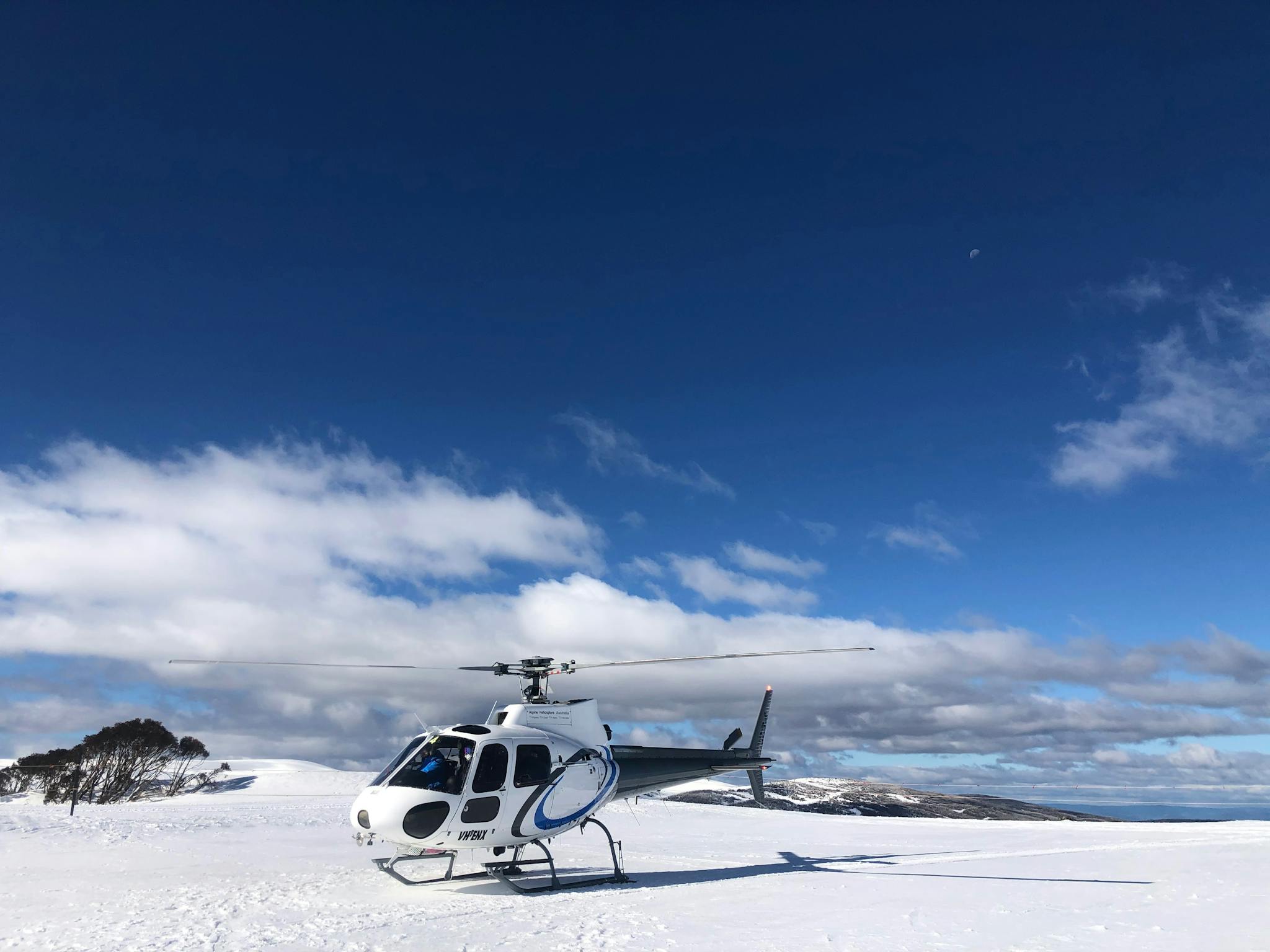 A helicopter parked on top of a snow covered mountain.